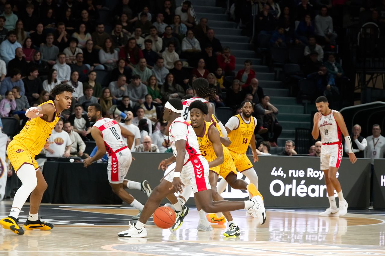 About Players in action during an indoor basketball game, with a crowd watching intently.