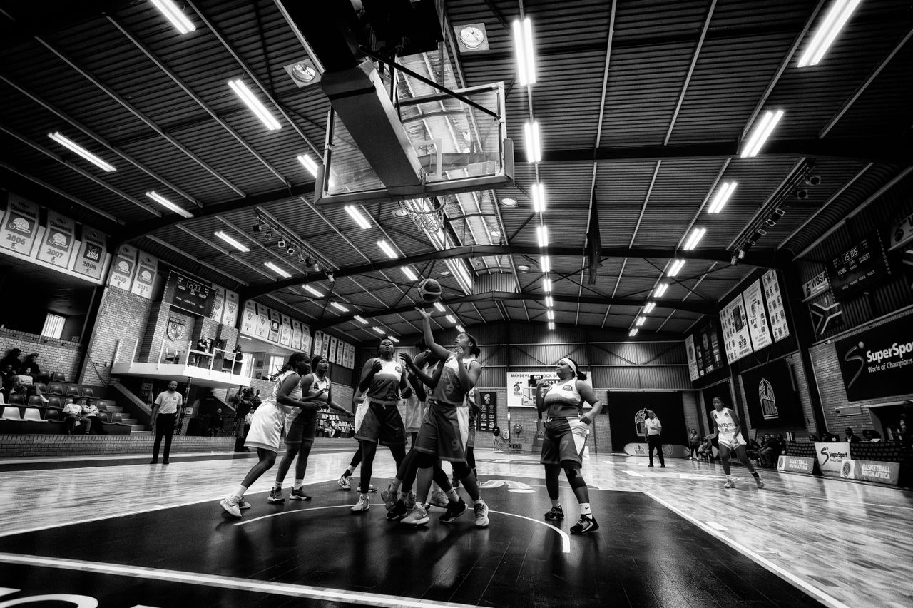 Services Dramatic indoor basketball game scene in Johannesburg, capturing athletes competing intensely under bright lights.